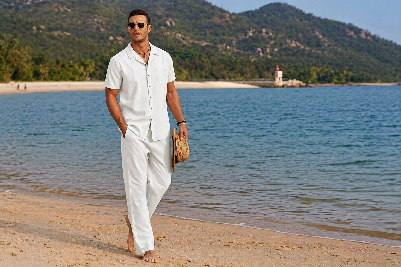 Man in white outfit walking on a beach with mountains and a lighthouse in the background