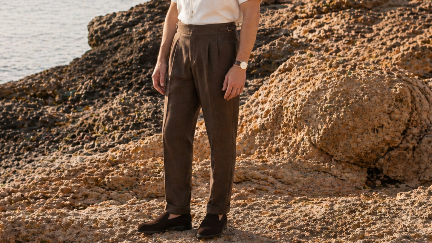 Person wearing brown pleated pants standing on a rocky beach.
