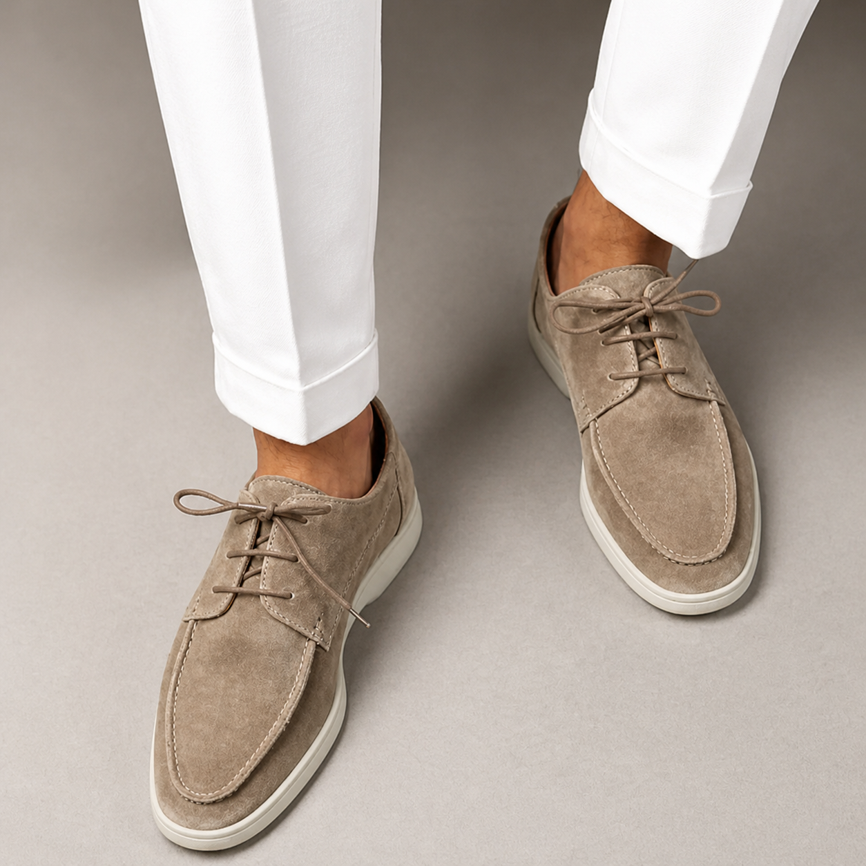 Beige suede shoes worn with white pants on a neutral background