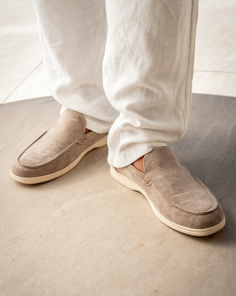 Beige loafers worn with white pants on a neutral background