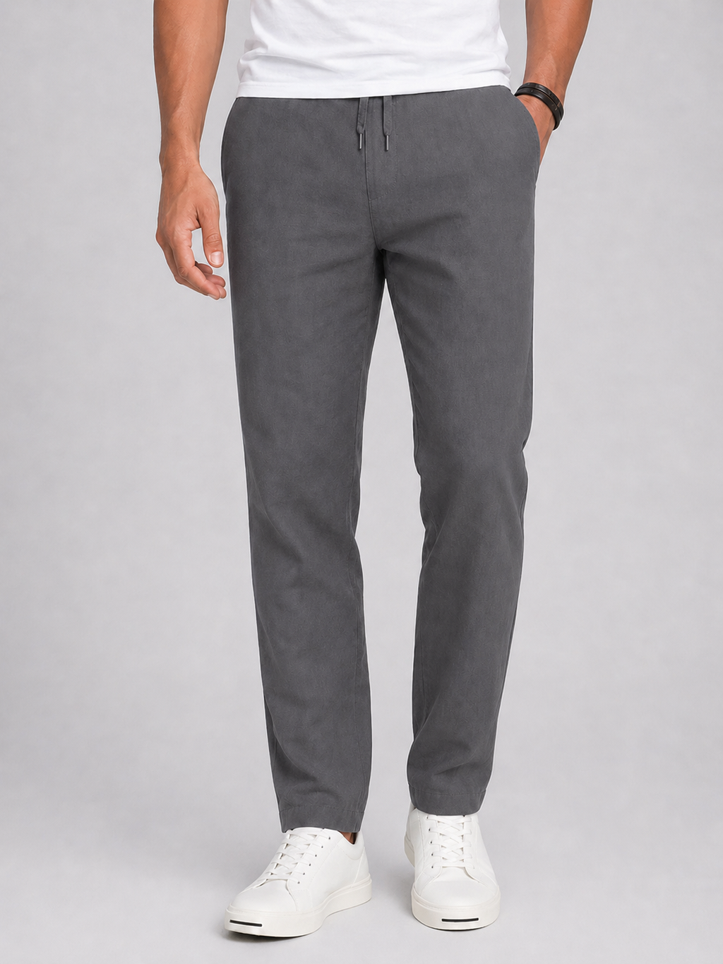 Person wearing gray pants and white sneakers on a plain background