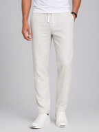 Men's light beige linen drawstring pants with a tapered leg and side pockets, paired with white sneakers.
