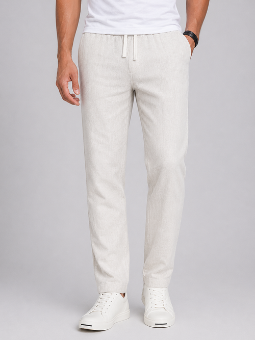 Men's light beige linen drawstring pants with a tapered leg and side pockets, paired with white sneakers.
