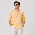 Men's mustard yellow linen long sleeve button-up shirt with rolled sleeves, paired with light beige linen trousers.