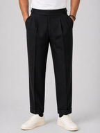 Men's black relaxed twin-pleat high-waist pants with side adjusters and cuffed hems.