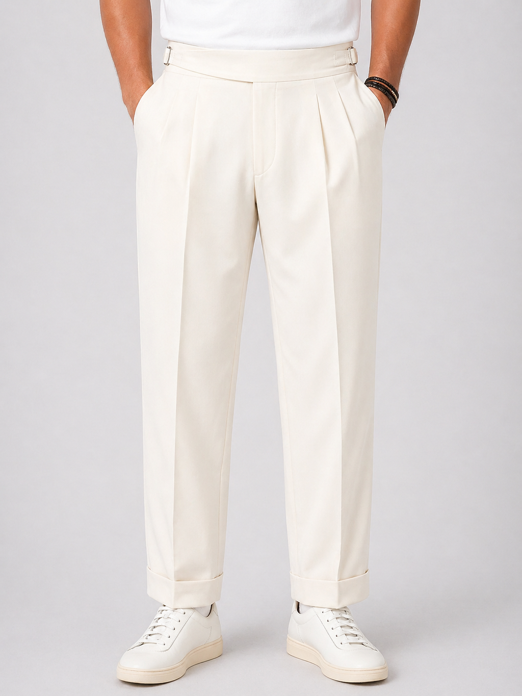 Men's relaxed fit, high-waist twin-pleat pants in cream, with side adjusters and cuffed hems.