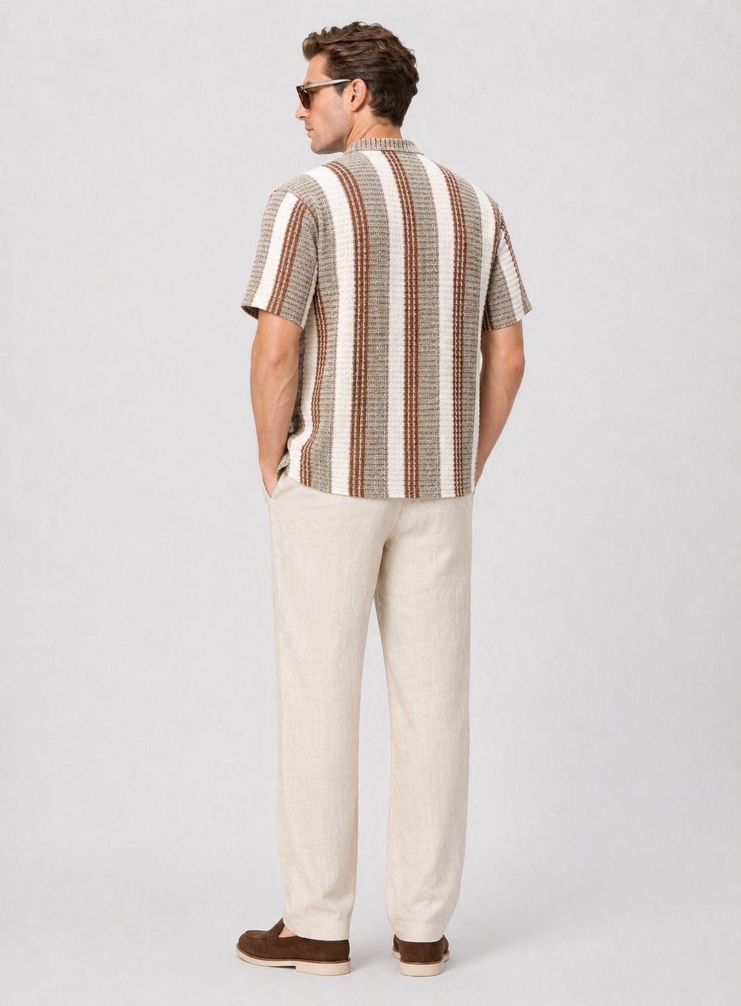 Men's short-sleeve striped shirt in brown and cream, paired with light linen trousers and brown loafers.