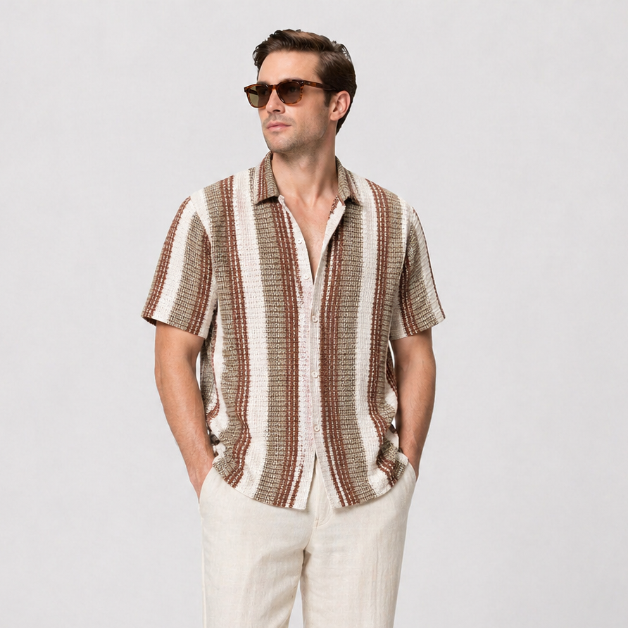 Men's short-sleeve striped shirt in brown, white, and tan, paired with light linen trousers and brown loafers.